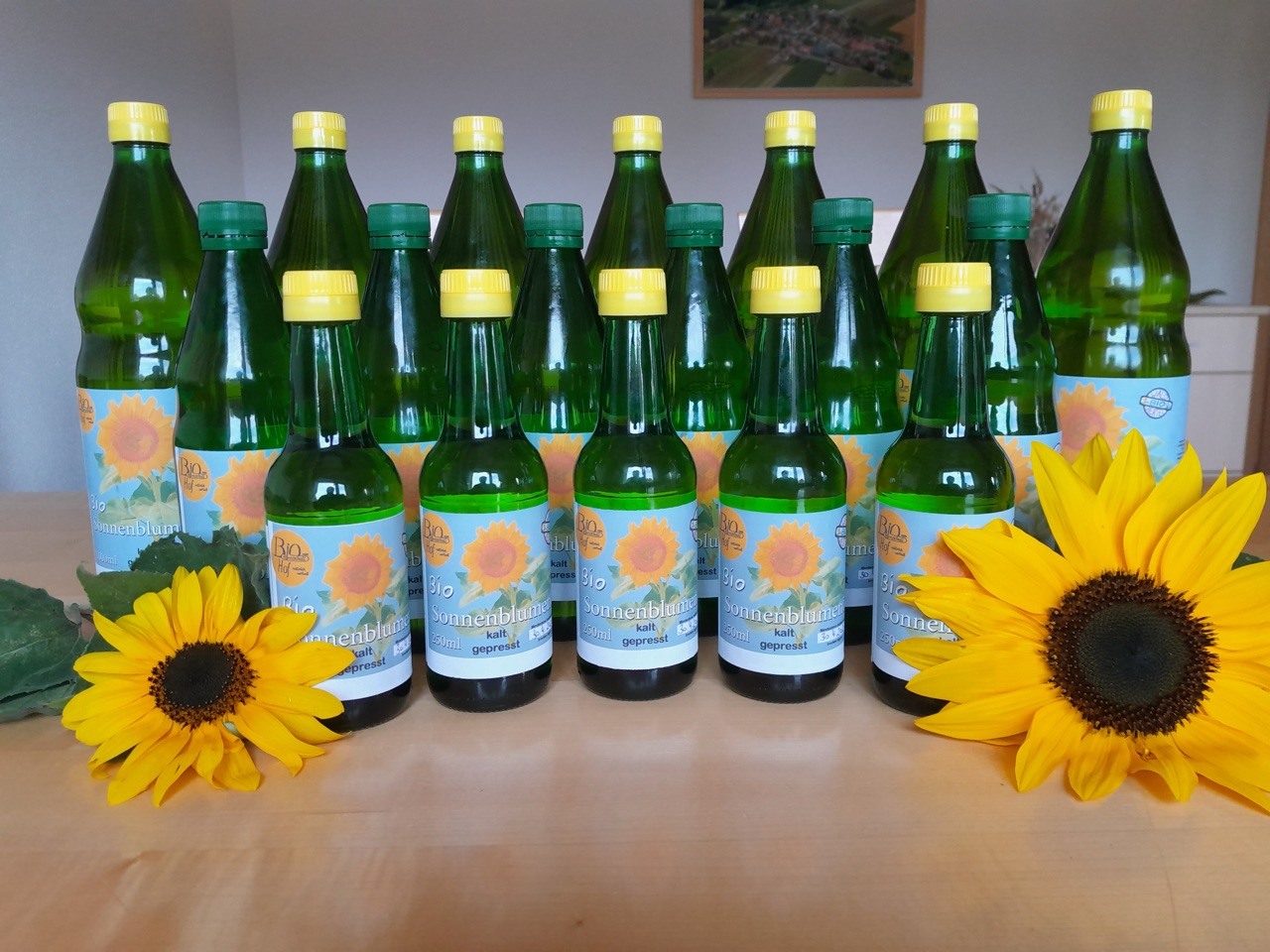 Flaschen mit kaltgepresstem Bio-Sonnenblumenöl vom Hof, daneben blühende Sonnenblumen